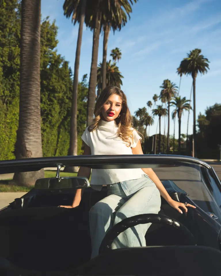 Tall palm trees against a clear blue sky above Nina in a vintage convertible
